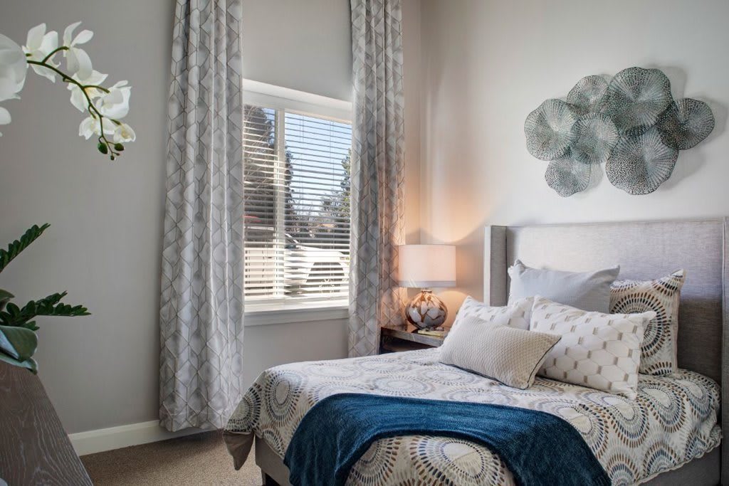 A cozy bedroom with a decorative bed, window with curtains, and a bedside lamp.