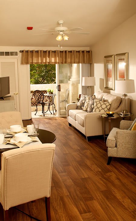 A cozy living room with modern furniture, wooden flooring, and decorative elements leading to a balcony.