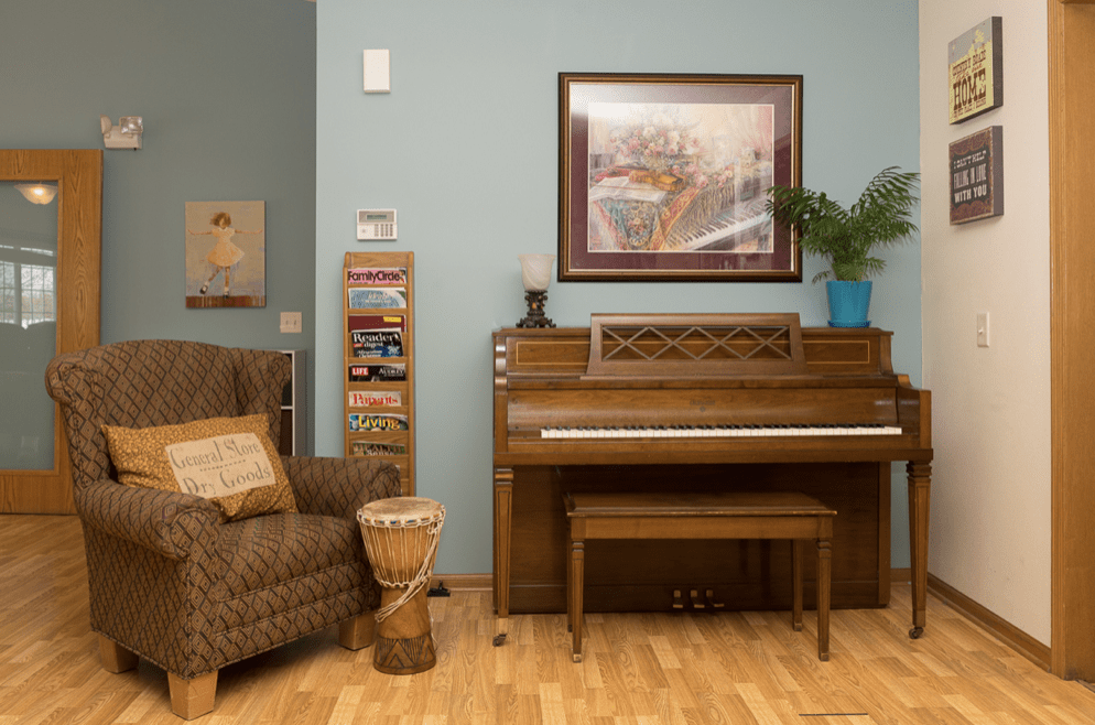 A cozy living room featuring a piano, armchair, and artwork on the wall.