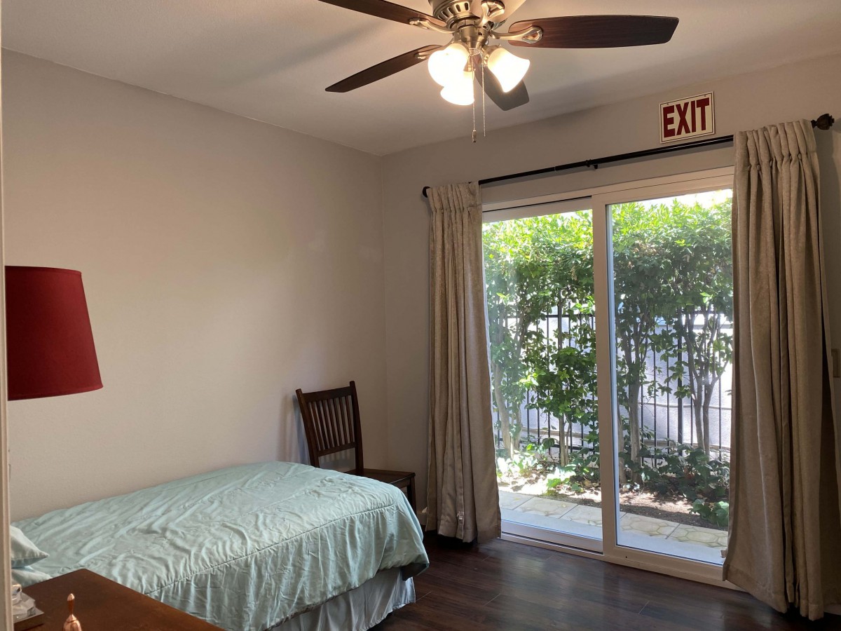 A cozy bedroom with a single bed, ceiling fan, and sliding glass door leading outside, allowing for natural light to fill the space.