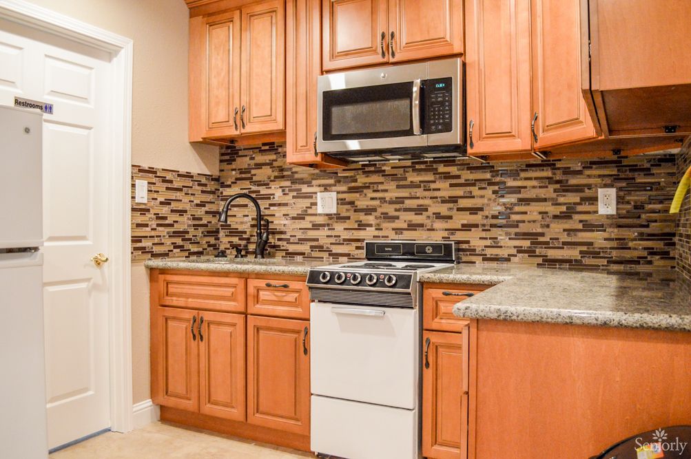 A cozy kitchen with wooden cabinets, a microwave, and a small stove against a decorative backsplash.