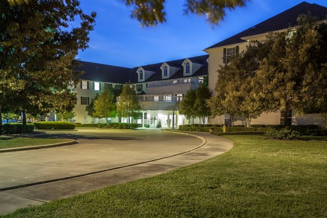 A well-lit building at night with surrounding trees and a circular driveway.