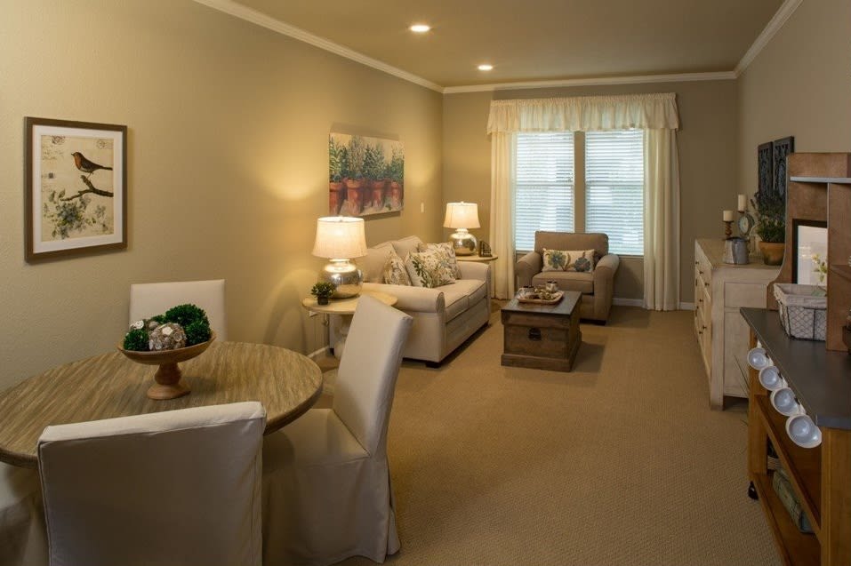 A cozy living room with neutral tones, featuring a sofa, armchair, coffee table, and decorative lamps.