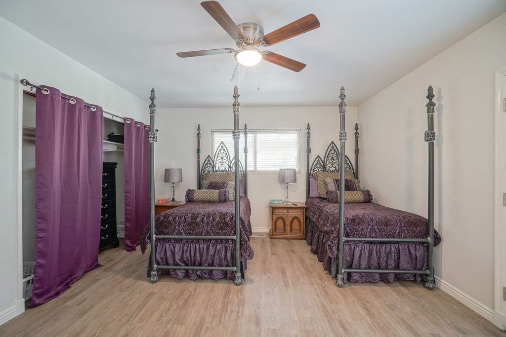 A bedroom with two ornate canopy twin beds, a ceiling fan, and wooden flooring.