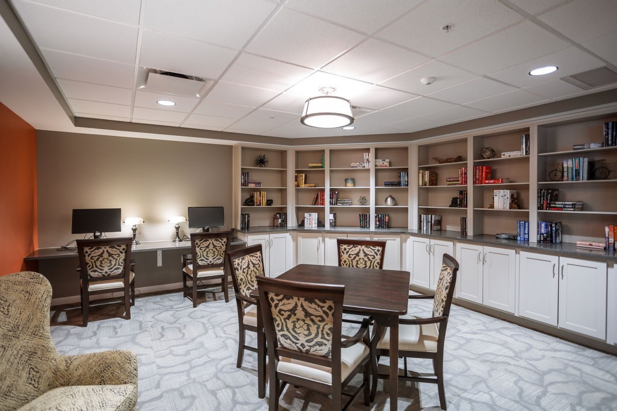 A well-organized study area featuring bookshelves, a central table surrounded by chairs, and computers along the wall.