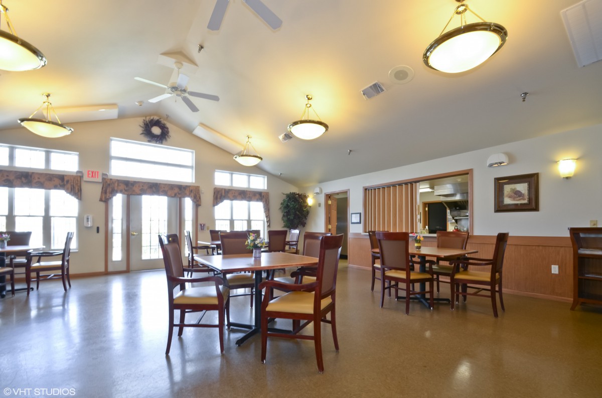 A spacious dining area with several tables and chairs, featuring ceiling fans and large windows.