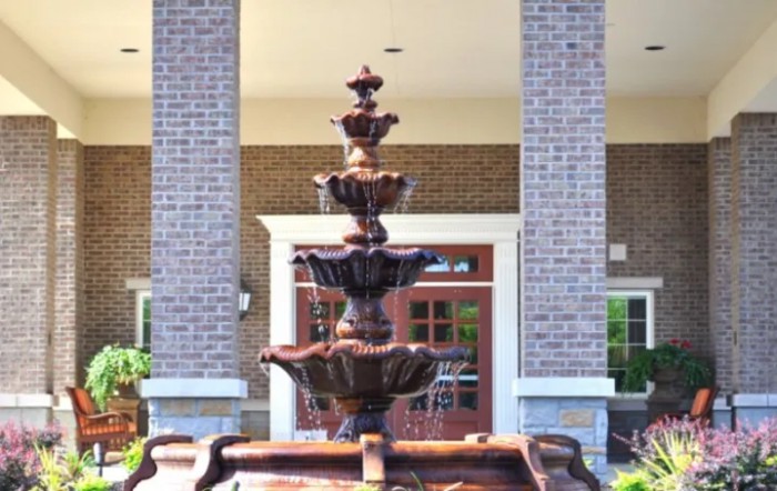 A decorative multi-tiered fountain in front of a brick building entrance.
