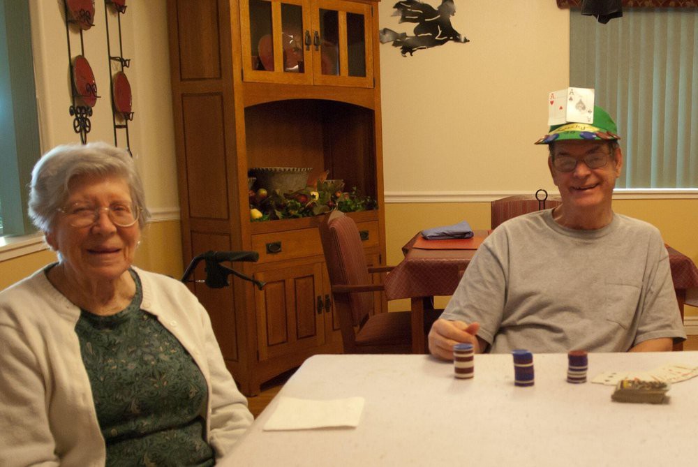 An elderly couple sitting at a dining table, smiling and enjoying a casual moment indoors.