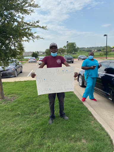 Two individuals in a parking lot, one holding a sign and the other wearing scrubs.