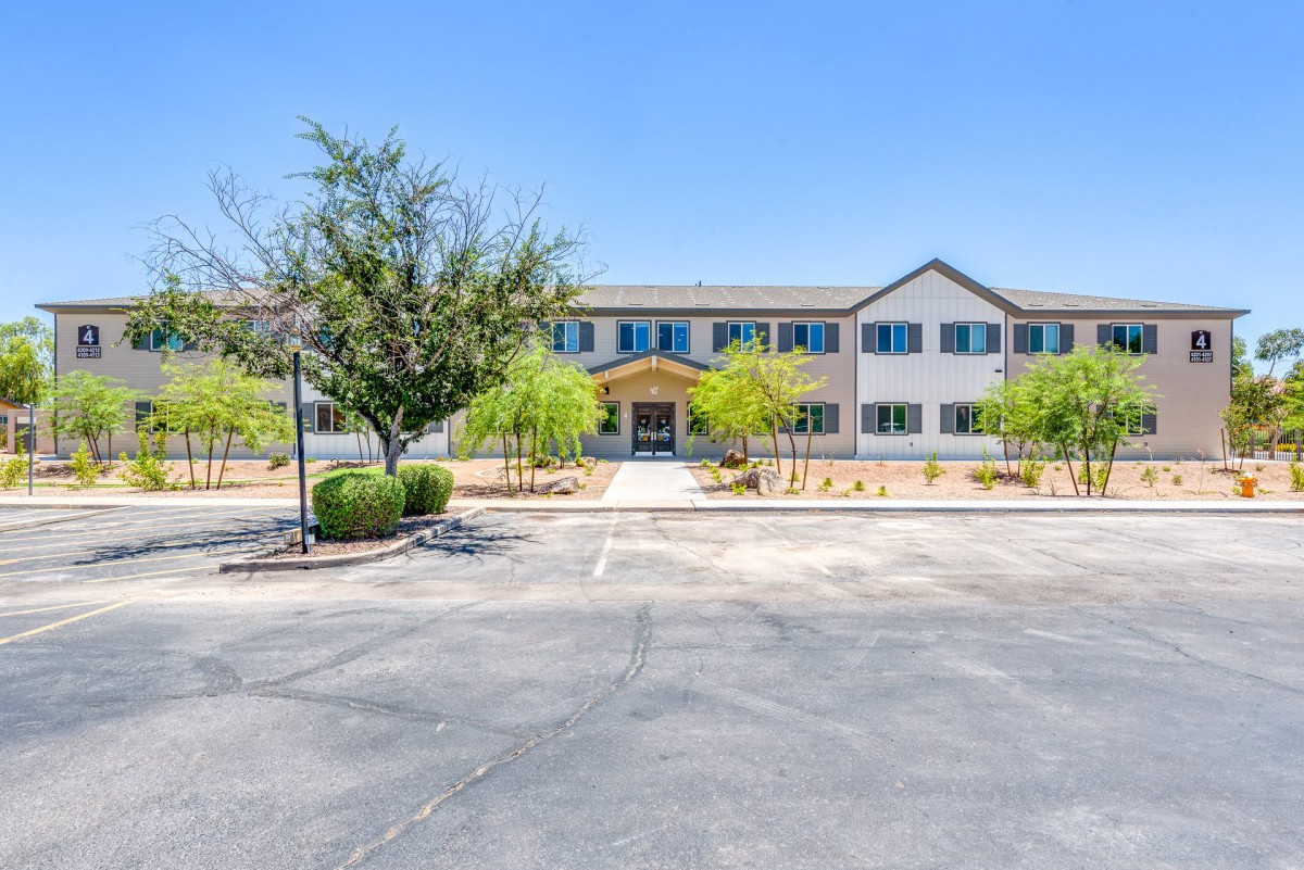 A view of a building with a parking lot and landscaped trees under a clear blue sky.