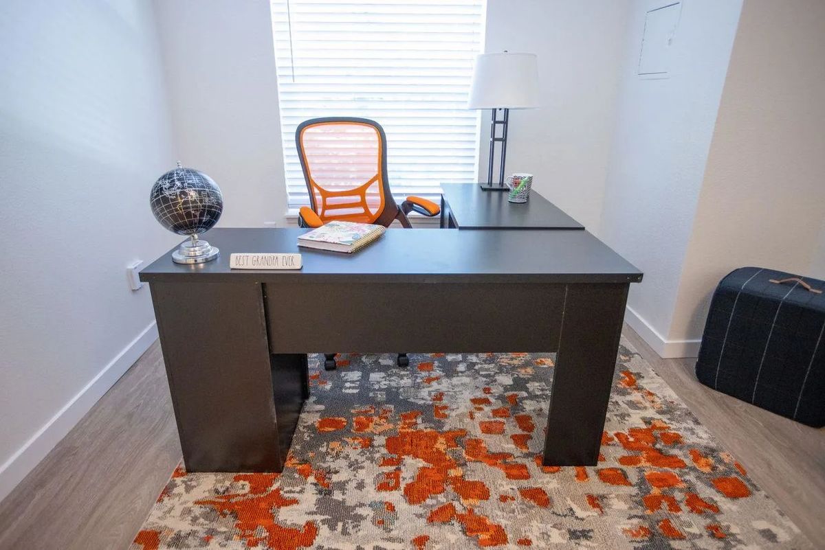 A modern home office setup with a black desk, orange swivel chair, and decorative rug.