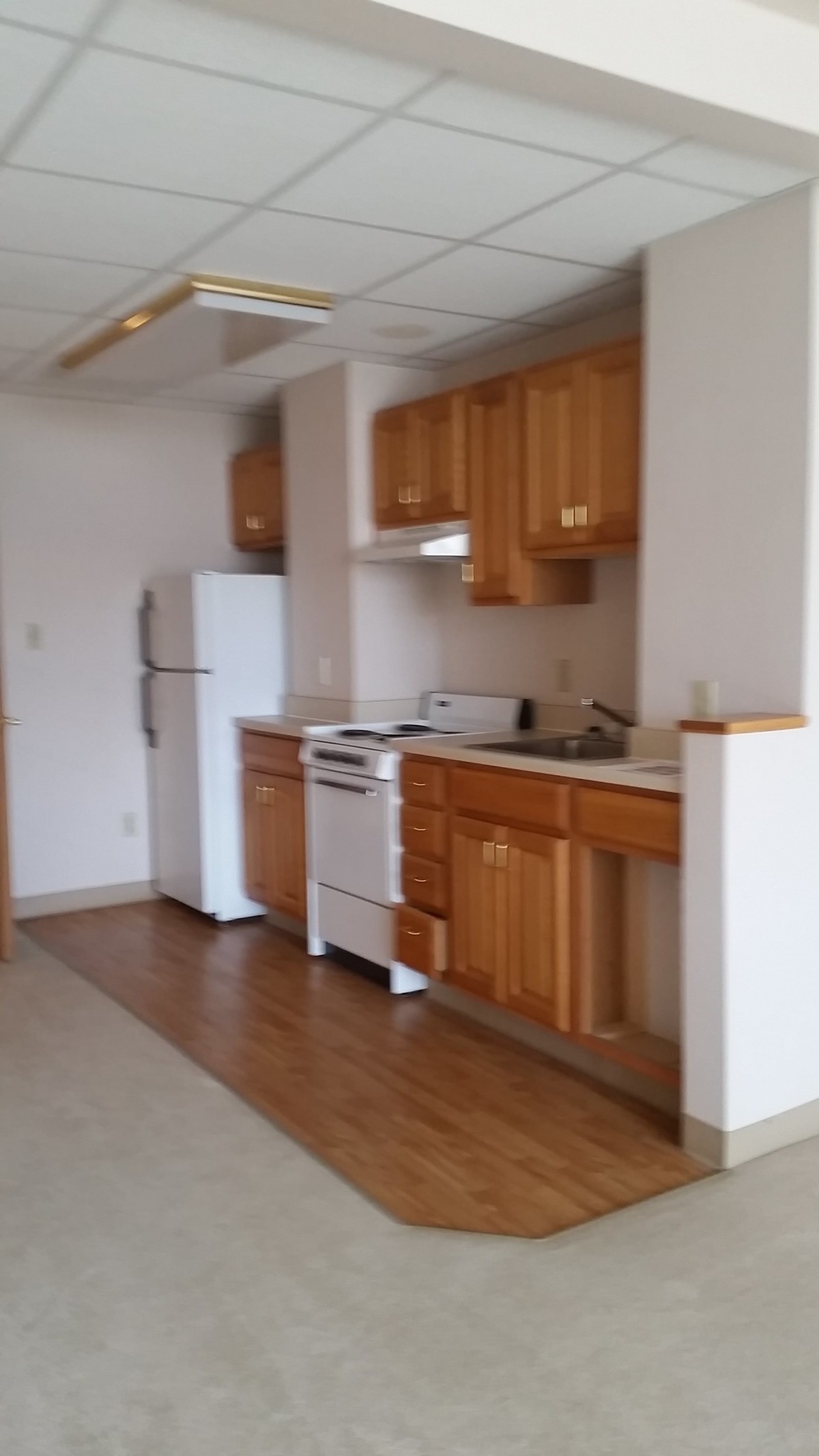 A simple kitchen with wooden cabinets, a refrigerator, and a stove.
