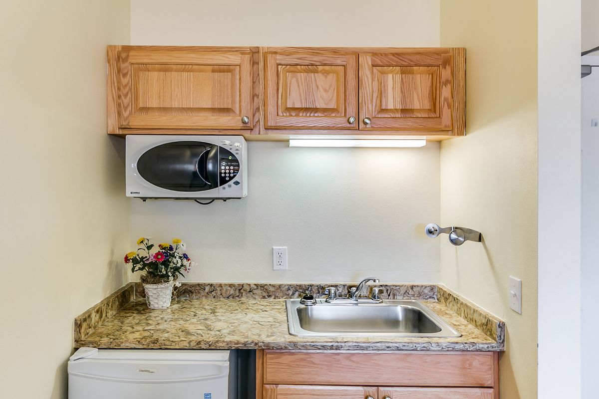 Compact kitchen area with wooden cabinets, a microwave, and granite countertop.