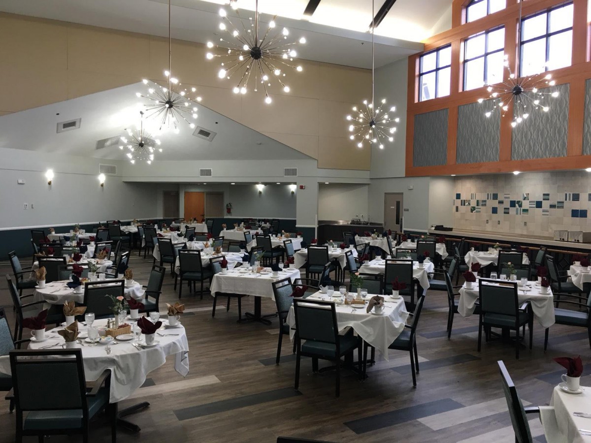 A spacious and elegantly designed dining hall with set tables and modern chandeliers.