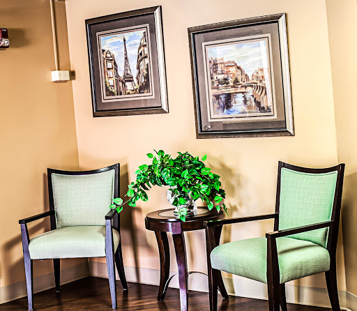 A cozy waiting area featuring green chairs, a small table with a plant, and framed artwork on the walls.