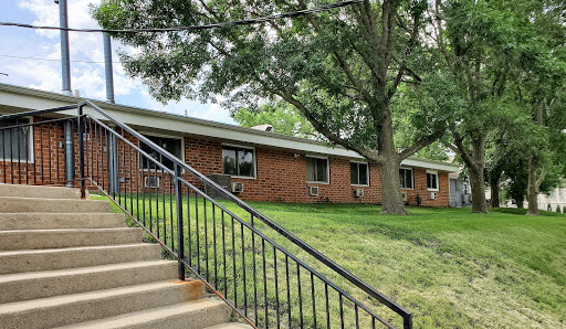 A view of a brick residential building with stairs leading up to it, surrounded by lush green grass and trees.