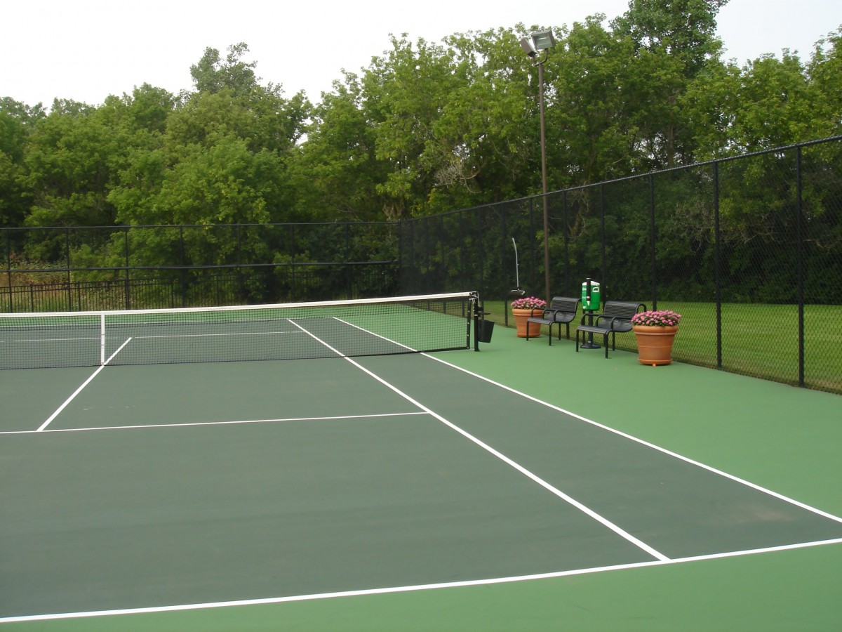 An outdoor tennis court surrounded by lush greenery.