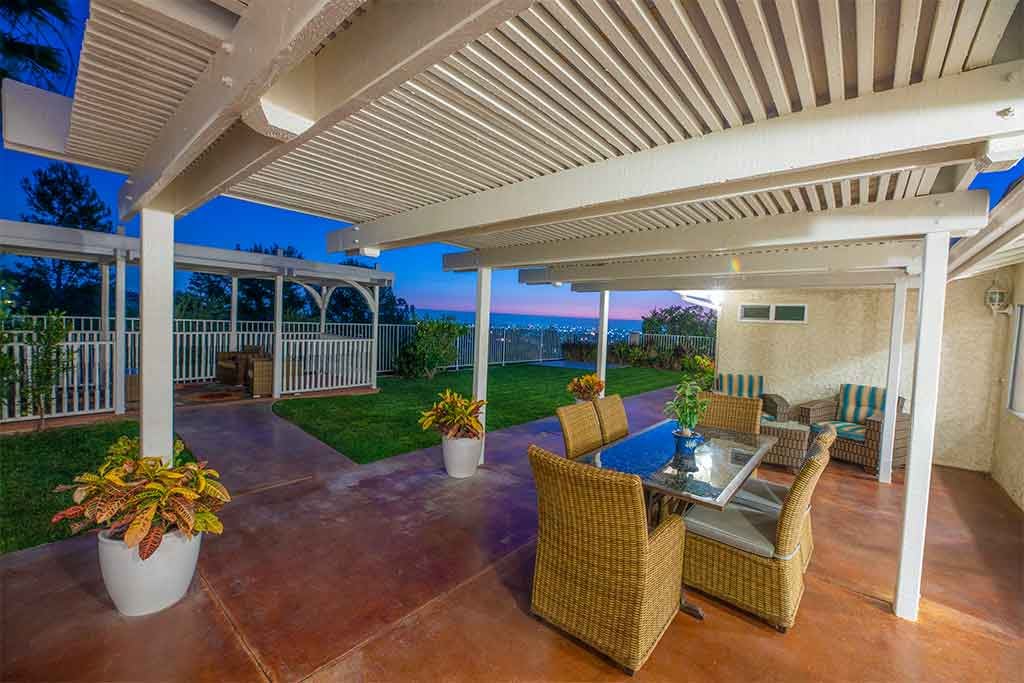 A cozy patio area with wicker furniture and a glass table, overlooking a scenic sunset.