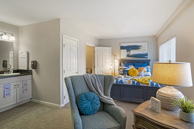 A cozy bedroom with a modern design, featuring a blue armchair, stylish bedding, and abstract artwork.