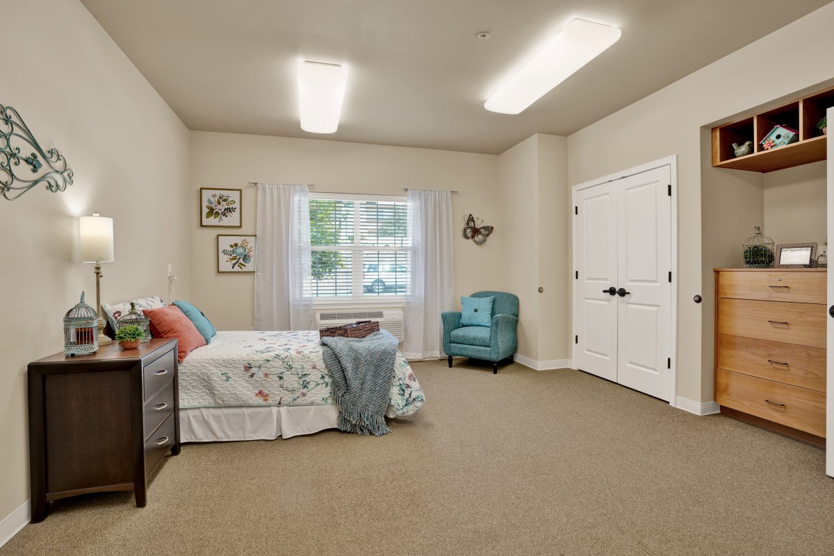 A cozy bedroom featuring a bed with floral bedding, an armchair, and a large window.