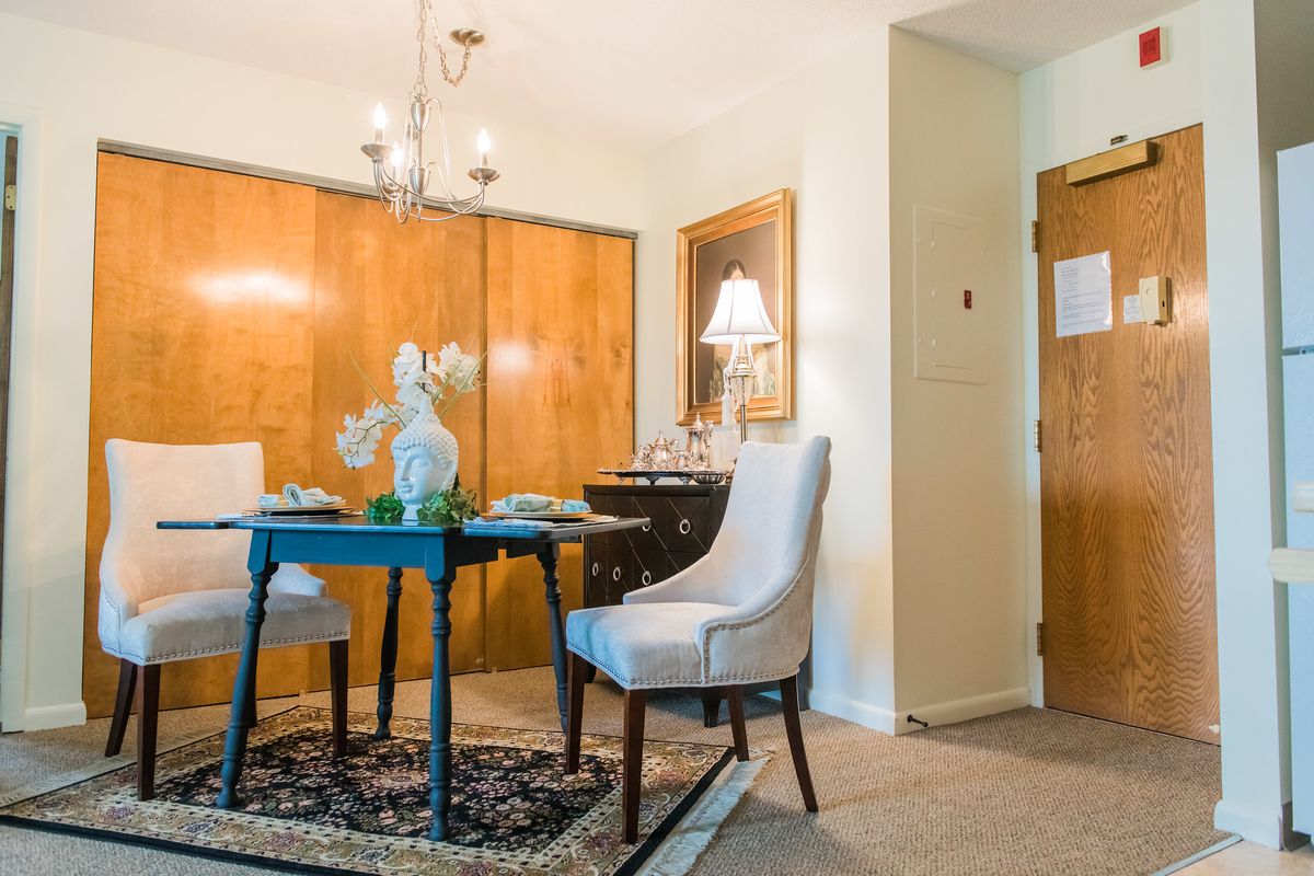 A cozy dining room with a round table and upholstered chairs, illuminated by a chandelier.