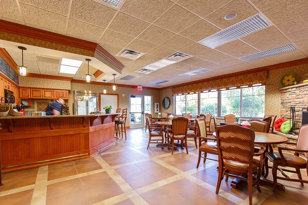 A welcoming dining area with wooden tables and chairs, filled with natural light from large windows.