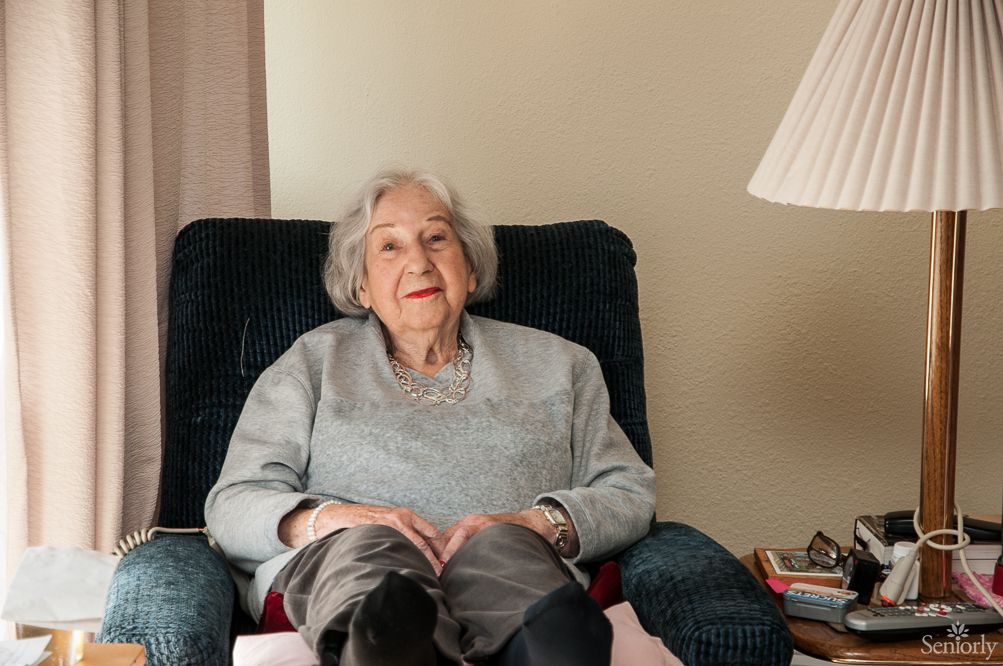 An elderly woman sitting comfortably in a living room chair.