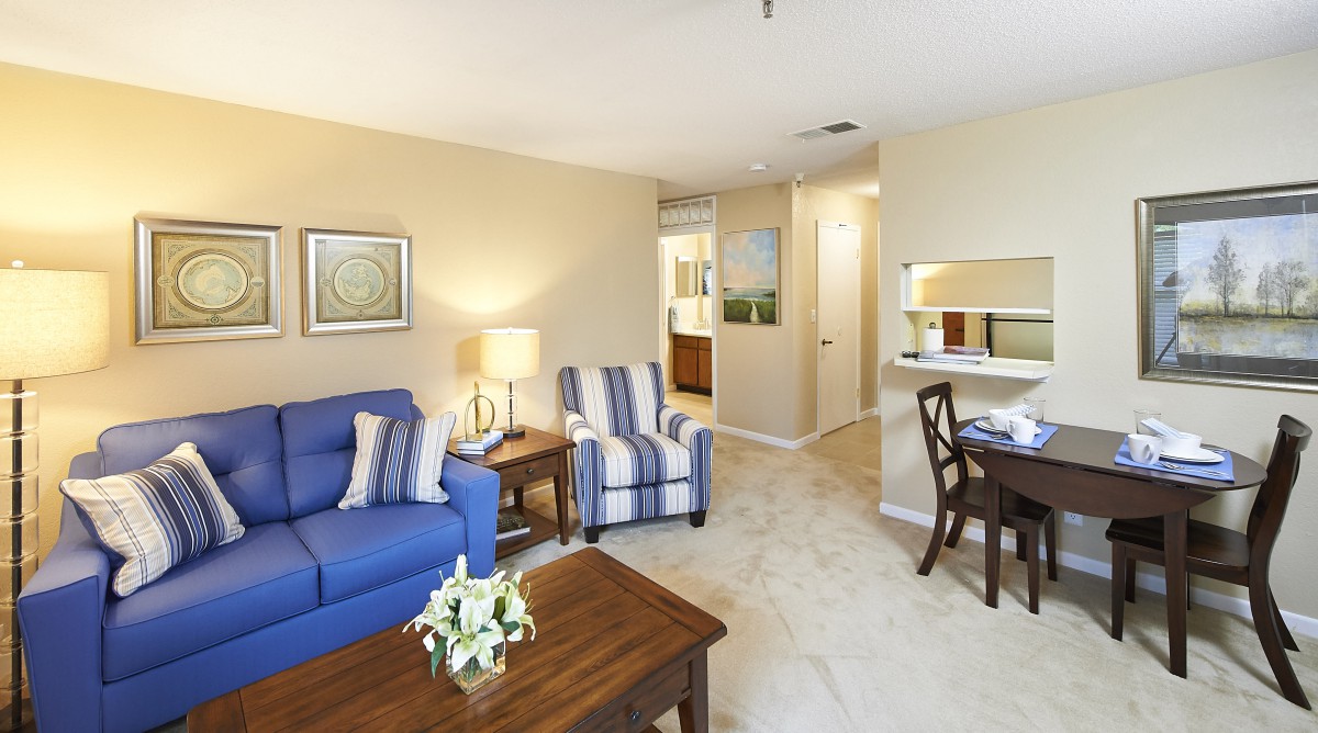 A cozy living room with a blue sofa, striped armchair, wooden coffee table, and soft lighting.