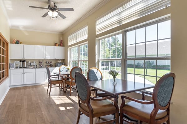 A bright dining space with large windows, featuring a table set and access to a kitchen area.