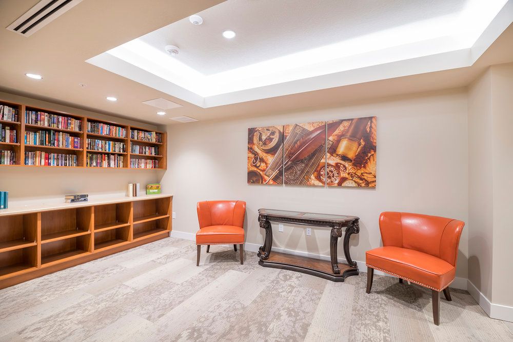 A modern interior space featuring orange chairs, a wooden console table, a bookshelf, and abstract wall art.