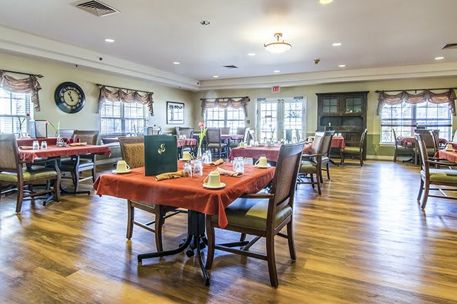 A cozy dining room with neatly arranged tables and chairs, featuring wooden floors and large windows.