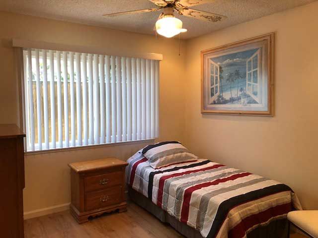 A cozy bedroom with a single bed and wooden furniture, featuring striped bedding and a ceiling fan.