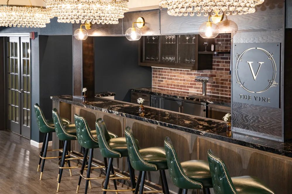 A stylish bar interior featuring green chairs and elegant lighting fixtures.