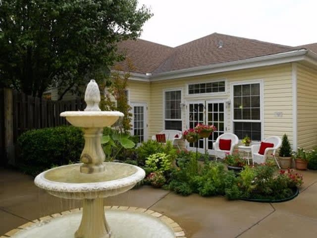 A charming patio area with a fountain, surrounded by lush greenery and outdoor seating.