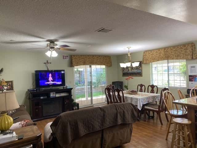 A cozy living and dining area with a television, ceiling fans, and large windows.