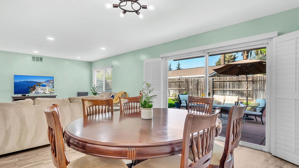 A spacious dining room with a wooden table and chairs, featuring a view through sliding glass doors to the outdoors.