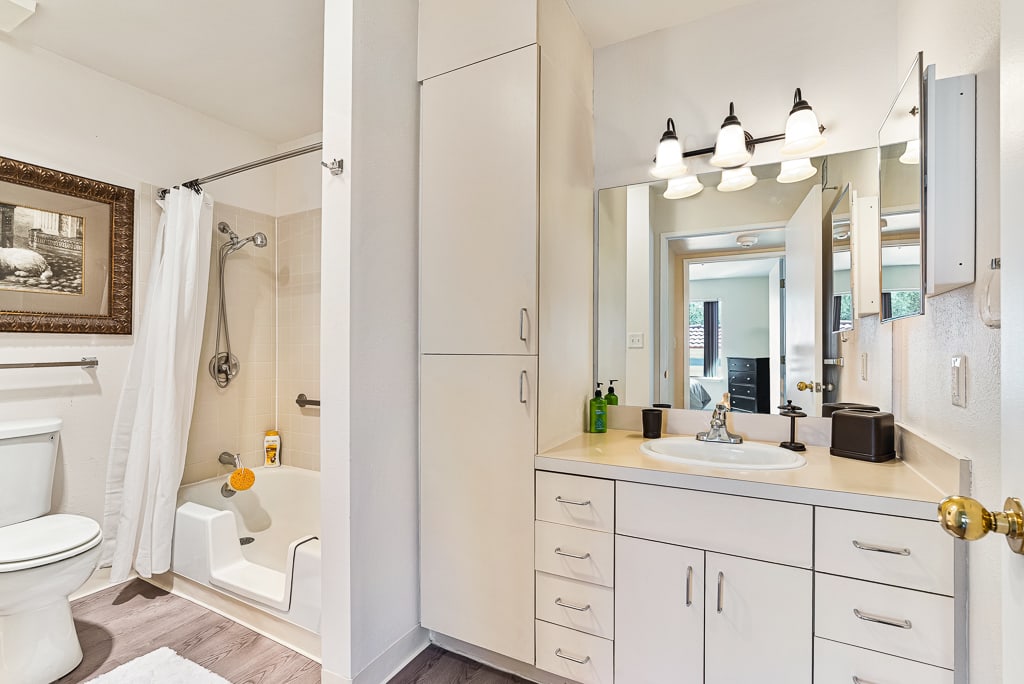 A modern bathroom interior featuring a vanity with a mirror, ample lighting, and a bathtub with a shower curtain.