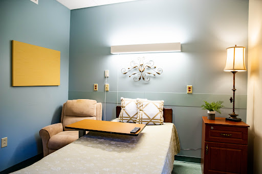 A well-lit hospital room featuring a patient's bed and a comfortable chair, adorned with decorative elements.