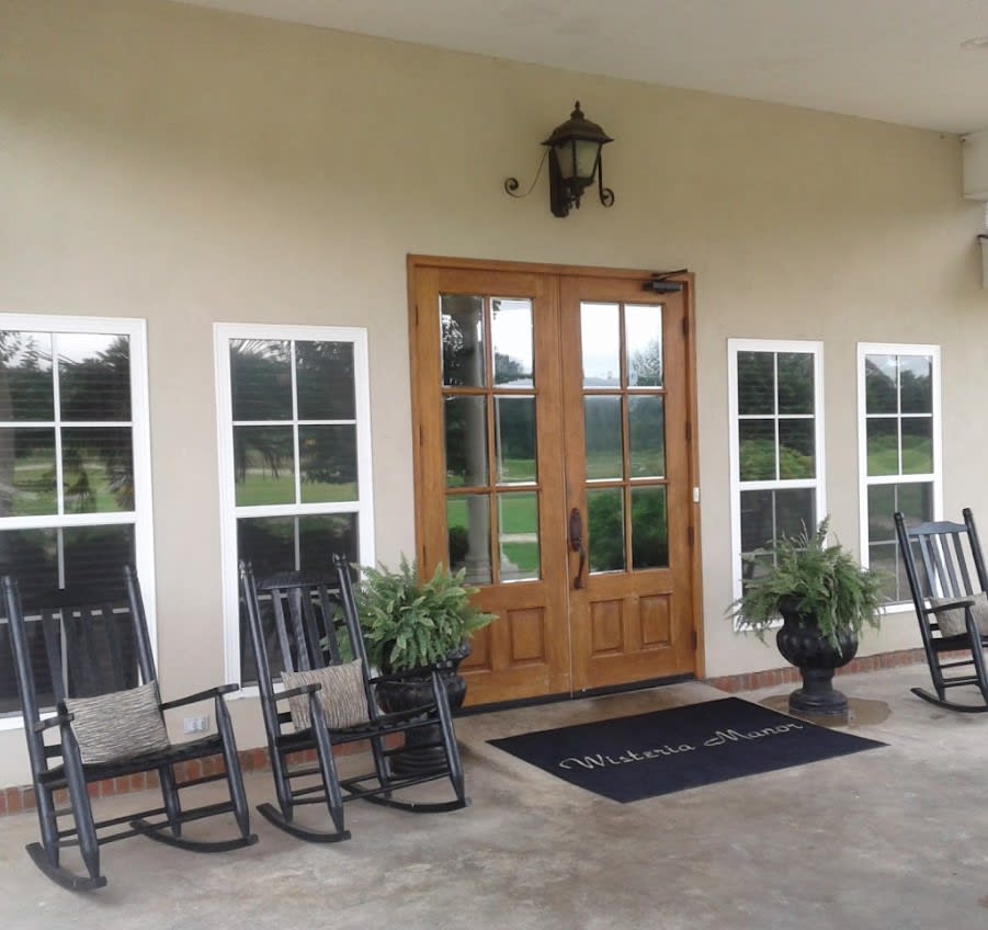 A welcoming front porch with wooden double doors, rocking chairs, and potted plants.