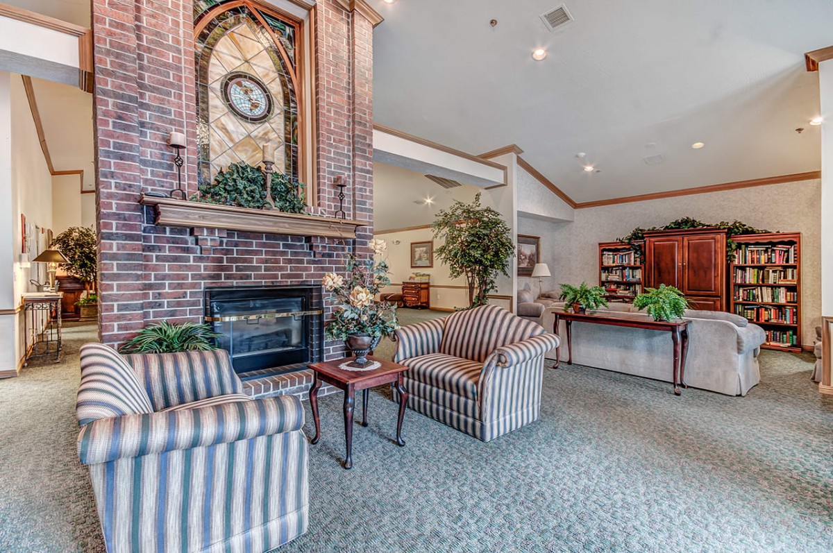 A cozy living room with a brick fireplace, striped chairs, and traditional decor.