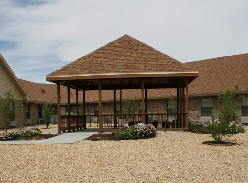 A wooden pavilion situated in a landscaped area with gravel and flowering plants.
