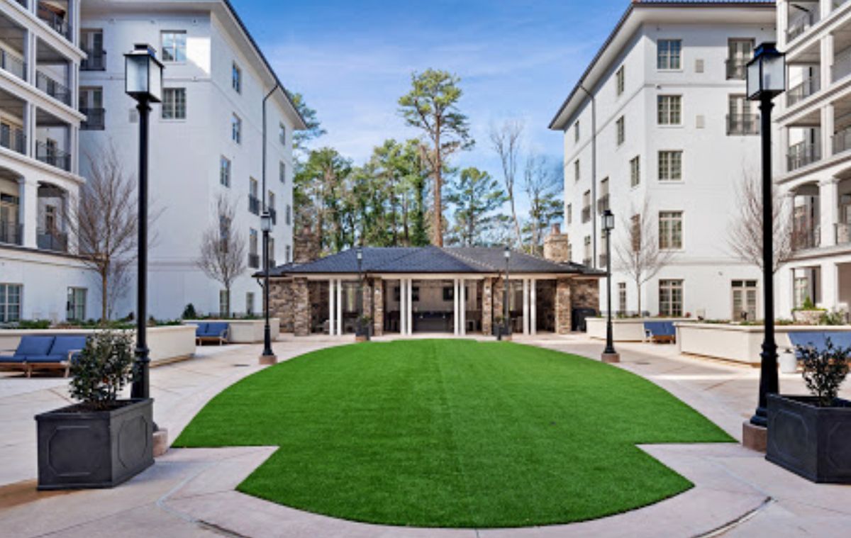 A neatly landscaped courtyard surrounded by buildings with a central grassy area and trees in the background.