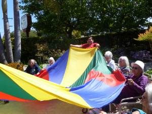 A group of seniors enjoying an outdoor parachute game on a sunny day.