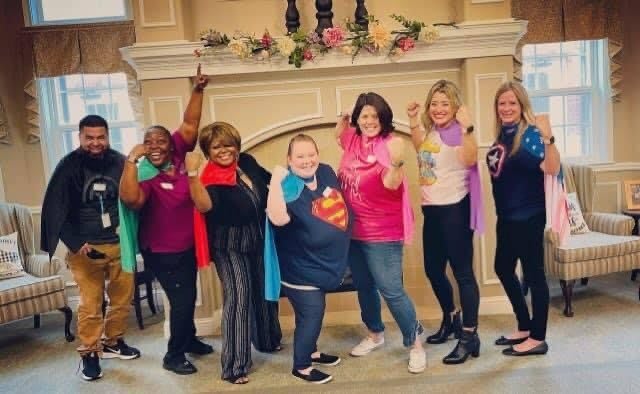 A group of women posing playfully with superhero capes indoors.