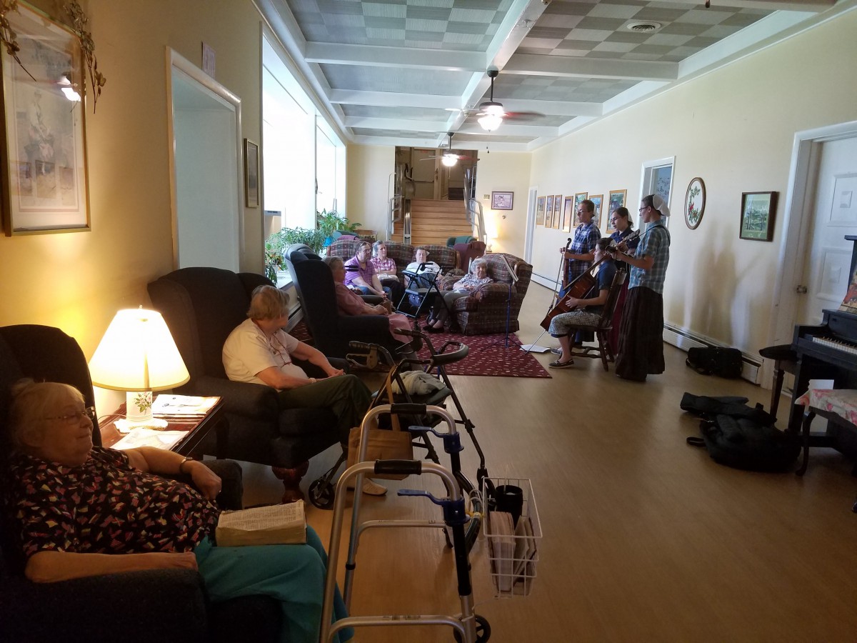 A relaxing common area in a nursing home with several elderly people seated and a walker nearby.