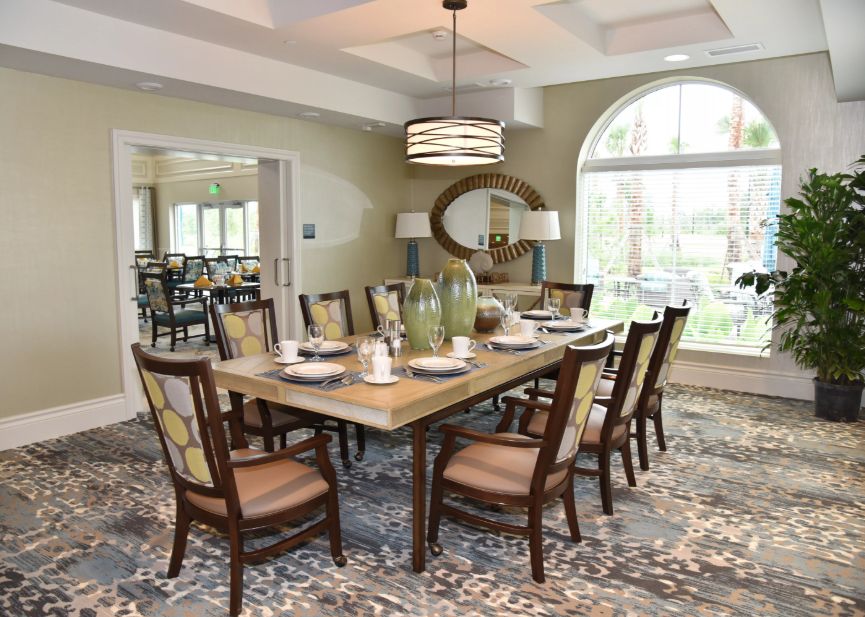 A well-decorated dining room with a large table and chairs, featuring a chandelier and a patterned carpet.