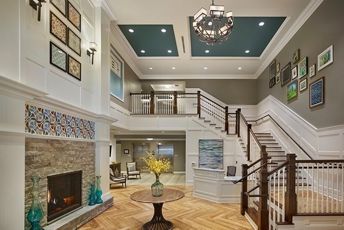 A luxurious and spacious living room featuring a grand staircase, modern decor, and a central chandelier.