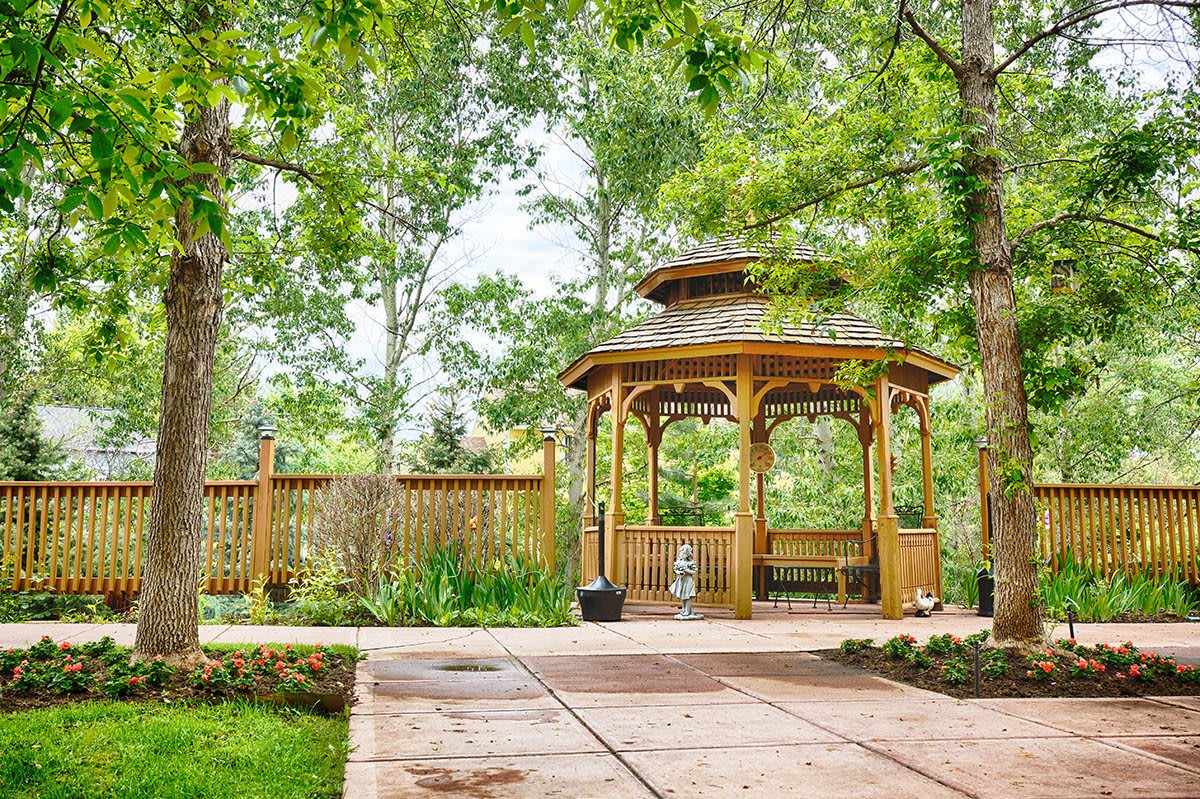 A serene garden featuring a wooden gazebo surrounded by lush greenery.