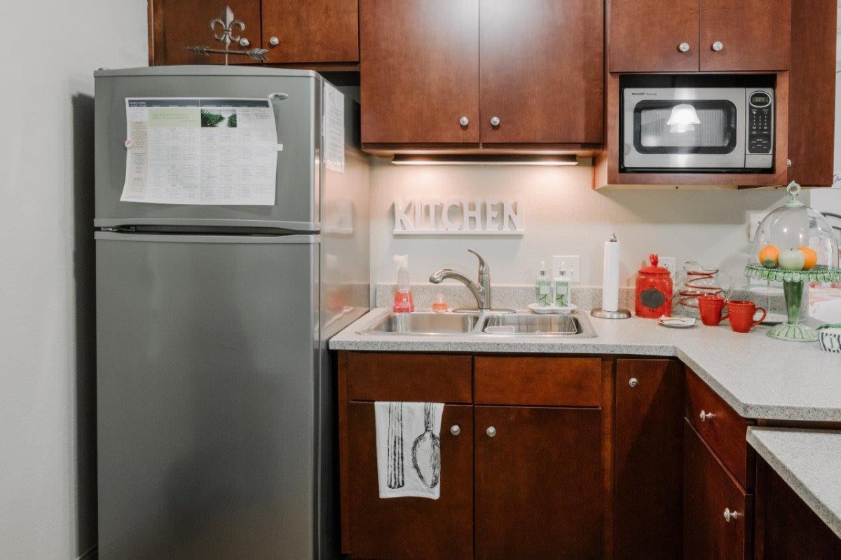 A compact kitchen area featuring a fridge, sink, microwave, and wooden cabinets.