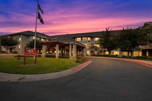 A hotel building at sunset with flags and a landscaped driveway.